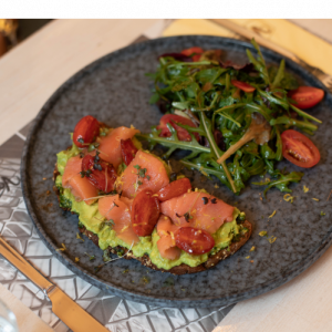 Open-faced salmon sandwich on toasted whole wheat bread with avocado mousse, rocket pesto, cherry tomatoes and basil oil